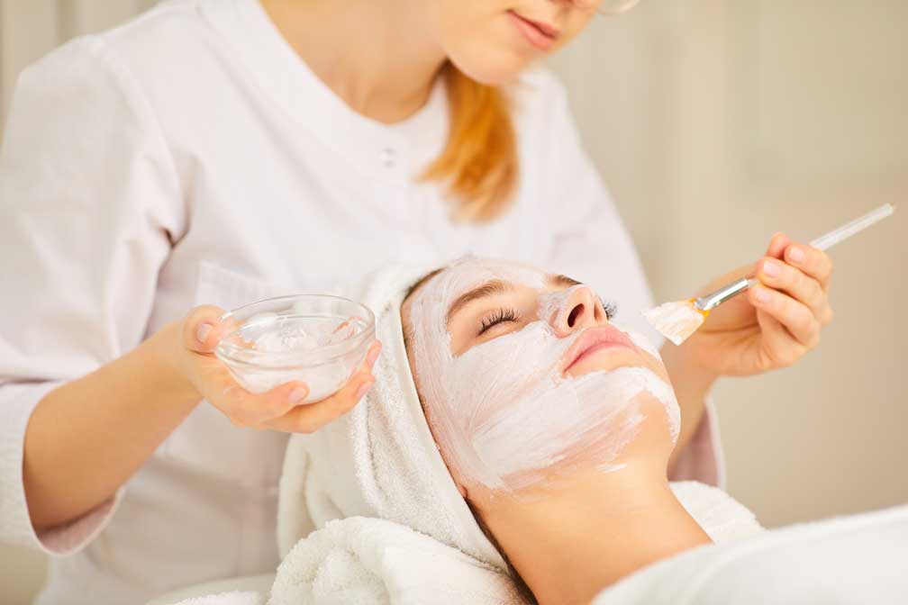 A cosmetologist applying facial mask to a woman